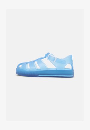 Sandale translucide albastre cu bretele decupate, curea la glezna și talpă texturată albastră. Design ușor și flexibil pentru confort.