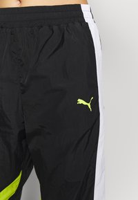 Black and white athletic pants with a neon yellow Puma logo on the right thigh worn by a person with bare midriff.