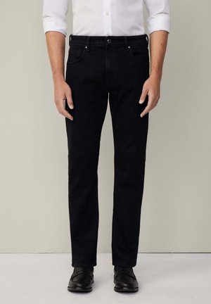 Schwarze Jeans aus Denim mit einer geraden Passform, Fünf-Taschen-Design und silbernen Hardware-Details, kombiniert mit einem weißen Hemd mit Knöpfen.
