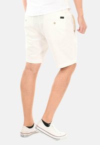 Herrenweiße Shorts aus Baumwolle mit einer soliden Textur. Verfügt über zwei Gesäßtaschen und Knopfverschlüsse. Trägt man mit weißen Sneakers.