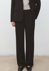 Czarne, dopasowane spodnie o prostym kroju nogawki, wykonane z gładkiej tkaniny. Noszone z jasnoszarym swetrem i ciemnymi butami.
