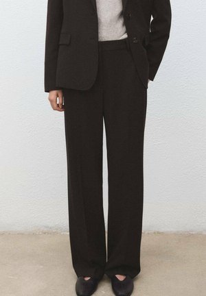 Czarne, dopasowane spodnie o prostym kroju nogawki, wykonane z gładkiej tkaniny. Noszone z jasnoszarym swetrem i ciemnymi butami.