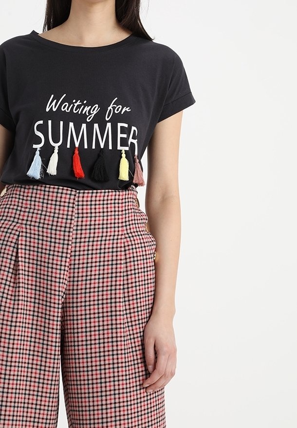 Černé tričko s krátkým rukávem a bílým nápisem "Čekání na LÉTO" a barevnými střapci. Růžové a černé kostkované kalhoty s vysokým pasem.