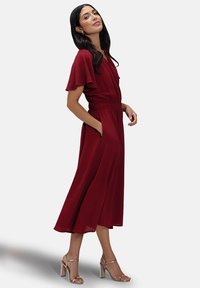 Burgundy midi-mekko, jossa on keveät hihat, joustava vyötärö ja sivutaskut. Valmistettu sileästä kankaasta; yhdistettynä metallisiin paljettikorkoisiin sandaaleihin.