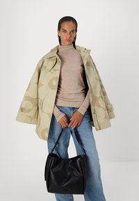 Beige mønstrete regnfrakk med oversized design, lagdelt over en tettsittende beige topp, kombinert med lyseblå jeans og en svart skinnveske.