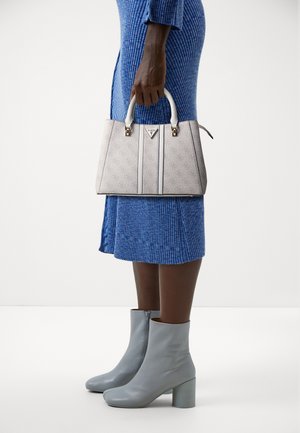 Personne portant une robe bleue côtelée et des bottines grises claires, tenant un sac à main blanc à motifs avec des doubles poignées.