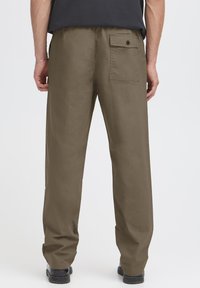 Pantalon kaki à coupe décontractée, doté d'une poche arrière unique avec fermeture à bouton, fabriqué en tissu texturé et durable.
