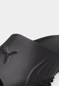 Μαύρο υφασμάτινο σανδάλι με λουρί, με ανάγλυφο λογότυπο Puma και σόλα με ακίδες για καλύτερο κράτημα.