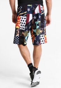 Flerfärgade shorts med ett lapptäckesdesign som har stjärnor, prickar och geometriska mönster i ett lätt tyg.