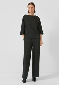 Een zwart, textuurstof outfit bestaande uit een losse top met brede mouwen en een wijde broek, aangevuld met spitse zwarte hakken.