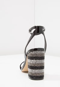 Svart lackläder-sandalett med ankelrem, med en hög, texturerad klack i blockform prydd med silver- och svarta rhinestones.