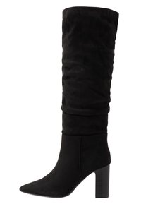 Bottes noires en daim montantes jusqu'au genou avec un design ample, un bout pointu et un talon épais. La texture est douce, offrant un aspect luxueux.