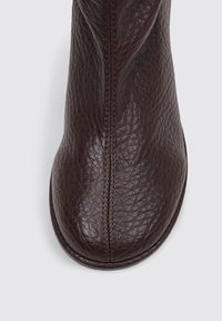 Bota de cuero marrón con un acabado texturizado, punta redondeada y detalles de costura que recorren verticalmente la parte delantera. Sin herrajes visibles.