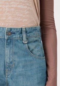 Jeans albaștri deschisi, cu talie înaltă, având cinci buzunare, un buton metalic și bucle pentru curea, cu o textură pronunțată de denim și o ușoară decolorare.