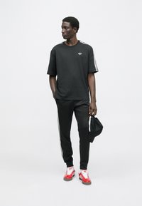 Čierne bavlnené tričko s krátkym rukávom a bielym logom Adidas, doplnené o čierne športové nohavice s bielymi pruhmi na bokoch a červené tenisky.