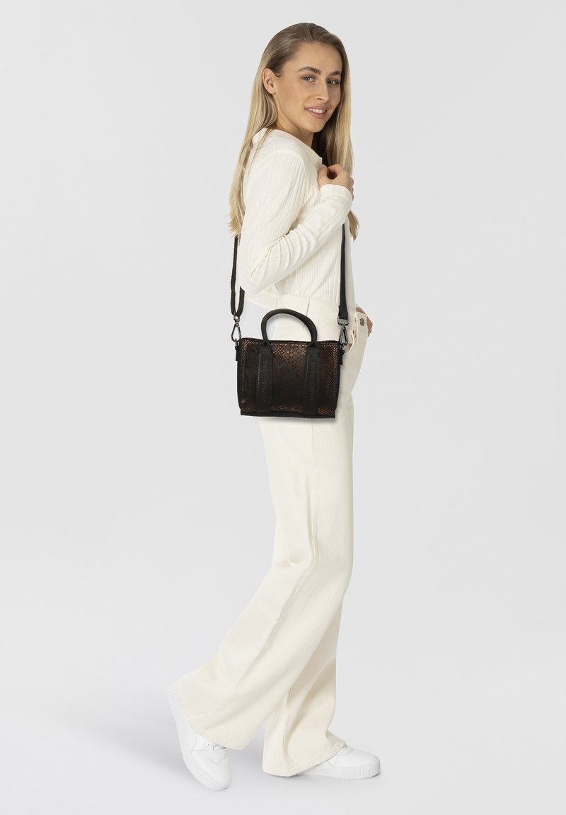Borsa a tracolla nera e marrone con manici superiori, cinturino lungo e regolabile, e pannelli laterali; abbinata a un outfit bianco e scarpe da ginnastica.