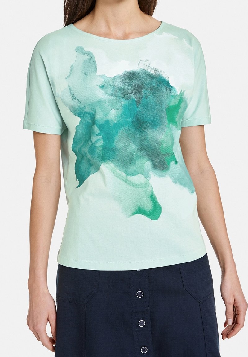 Camiseta de manga corta verde claro con un patrón abstracto de acuarela verde oscuro. Material de algodón suave con escote redondo y un corte relajado.