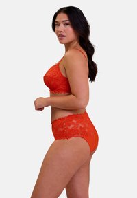 Conjunto de lencería de encaje en un vibrante color rojo. El sujetador cuenta con tirantes ajustables; las bragas de cintura alta tienen detalles de encaje y bordes en forma de ondas.