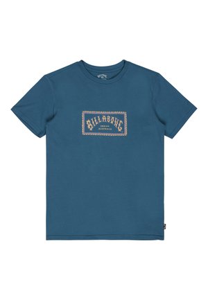 Niebieska koszulka z krótkim rękawem i okrągłym dekoltem z prostokątną naszywką z logo "Billabong Since 1973 Australia" na piersi.