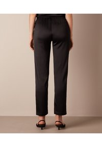 Svarta satinbyxor med elastisk midja, rak bendesign och en slät yta. Bärs med svarta klacksandaler.