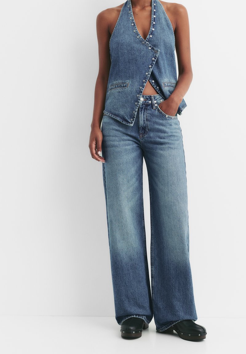 Denim halter top, svetlo modra, z gumbnimi detajli; kombinirani z širokimi svetlo modrimi kavbojkami, ki imajo visok pas in sprednje žepe.