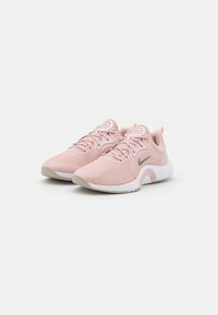 Un paio di scarpe da corsa Nike rosa con suole bianche e loghi swoosh grigi angolati su uno sfondo bianco.