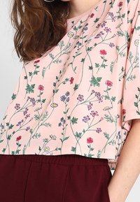 Ljust rosa cropped topp med ett blommönster i röda, lila och gula blommor. Mjukt tyg med en avslappnad passform och korta ärmar.