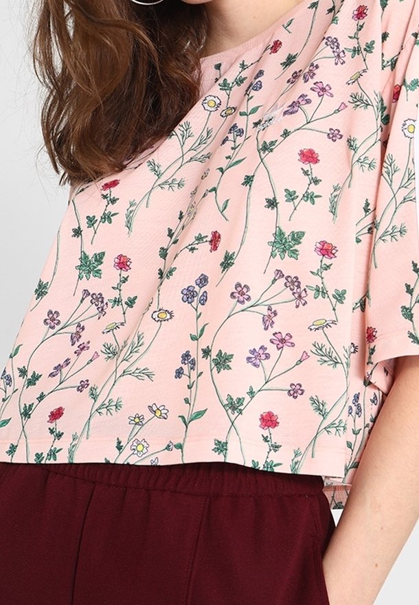 Ljust rosa cropped topp med ett blommönster i röda, lila och gula blommor. Mjukt tyg med en avslappnad passform och korta ärmar.