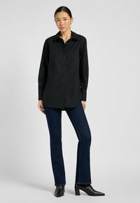 Zwarte overhemd met lange mouwen, klassieke kraag en rechte snit, gecombineerd met donkerblauwe flared jeans en zwarte hielenlaarzen.