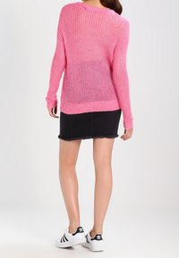 Rosa gestrickter Pullover mit langen Ärmeln, lockerer Maschenart und weitem Ausschnitt, kombiniert mit einem schwarzen Jeansrock mit fransigem Saum.