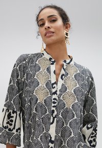 Camicia bianca e nera con motivo floreale, design button-down e dettagli ricamati. Presenta maniche a tre quarti e una texture morbida.