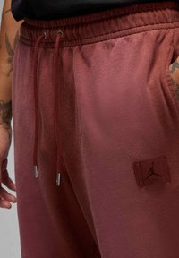 Bordeauxfarbene Jogginghosen aus weichem Stoff mit elastischem Bund, Kordelzug mit Metallenden und einem Logopatch an der Seite.