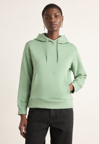 Ljusgrön hoodie med en känguruficka, justerbara dragsnören och ribbade ärmslut. Har en liten, subtil logotyp på bröstet.