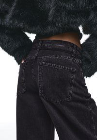 Jean noir taille haute en denim, avec une coupe droite, des poches arrière, et une ceinture de marque avec une finition texturée.