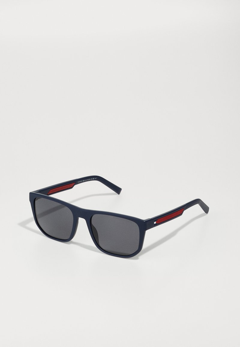 Navy blue sunglasses with square frames, dark lenses, and red accents on the sides. Made of lightweight plastic with smooth texture.