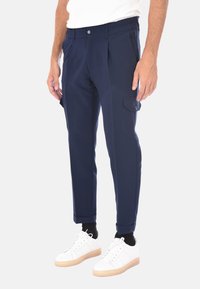 Pantaloni blu navy con vestibilità rilassata, davanti plissettato e tasca laterale; realizzati in tessuto morbido, abbinati a sneakers bianche.