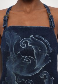 Τζιν τοπ με σκούρο μπλε ύφασμα, ρυθμιζόμενους ώμους με χρυσές λεπτομέρειες και περίπλοκο απαλό σχέδιο μπροστά.