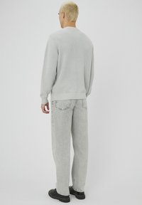 Pull en tricot gris avec un col rond, associé à un jean gris clair, ample. Des chaussures noires complètent la tenue. Design simple, texture lisse.