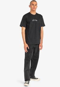 Black cotton t-shirt with a crew neckline and a small, white graphic on the chest, paired with dark gray jeans and black sneakers.
