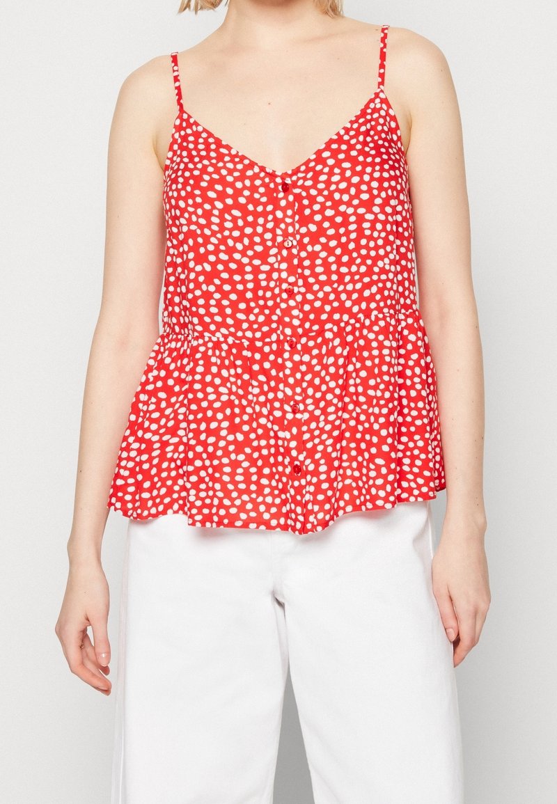 Top sin mangas rojo con lunares blancos, escote en pico, cierre de botones en la parte delantera y dobladillo peplum. Tela ligera con una textura suave.