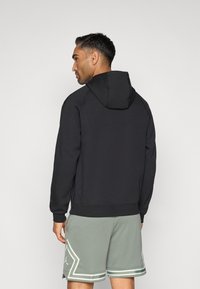 Μαύρο φούτερ με κουκούλα και κορδόνι, με ριγωτούς μανίκους και τέρμα, σε συνδυασμό με γκρίζα αθλητικά σορτς με διάτρητη υφή και αντίθετες λεπτομέρειες.