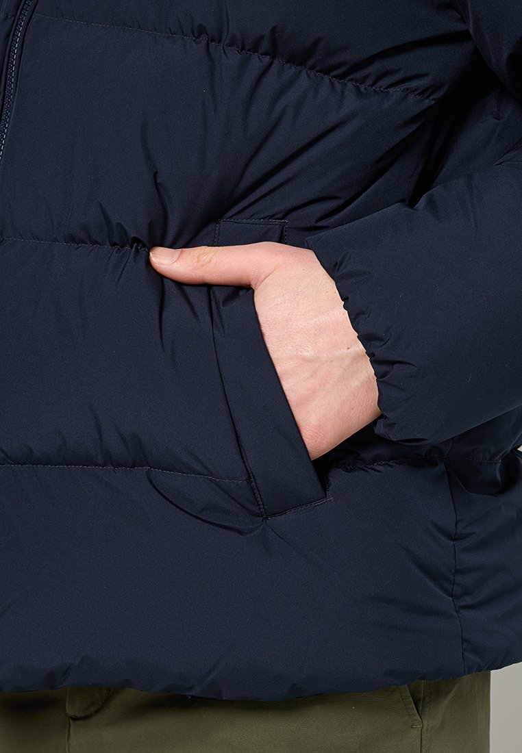 Granatowa kurtka puchowa z wyraźnym pikowanym wzorem, boczna kieszeń na ręce oraz gładka, syntetyczna tekstura. Widoczne zapięcie na zamek.