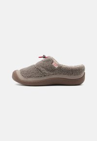 Clog fuzzy gri din material moale, cu vârf rotunjit, talpă robustă de culoare maro și detaliu cu buclă roșie pentru ajustare ușoară.