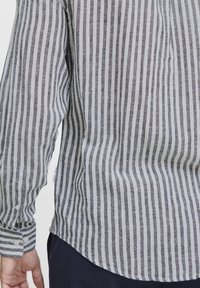 Langermet skjorte i lett stoff med vertikale grå og hvite striper, med knapper på mansjettene og en buet hem.