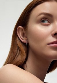 Srebrna minimalistyczna spiralna kolczyk przymocowana do płatka ucha, z wypolerowaną metalową powierchnią. Modelka ma czerwone włosy i gładką skórę.