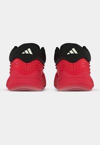 Un paio di scarpe sportive rosse e nere viste da dietro, con un logo bianco a tre strisce sul collo del tallone.