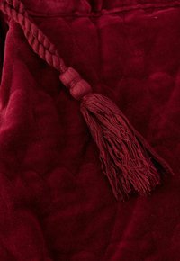 Diep rode gevlochten kwast met franjes rustend op een geplooide fluwelen stofachtergrond.