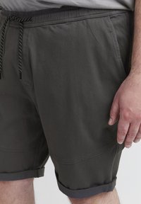 Dunkelgraue Shorts mit elastischem Bund, schwarz-weißer Schnur, umgeschlagenen Hosenbeinen und glattem Stoff mit verstärkten Nähten.