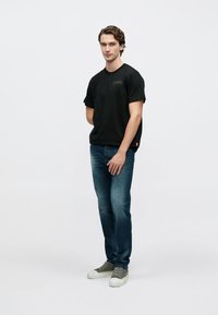 Camiseta de algodón negra con un pequeño logo, combinada con jeans de mezclilla azul y zapatillas verdes. El conjunto tiene un ajuste casual y relajado.