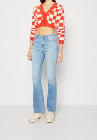 Virkat röd och vit rutigt kort cardigan, kombinerad med ljusblå utsvängda jeans och beige plattformsskor. Slät textur, avslappnad stil.